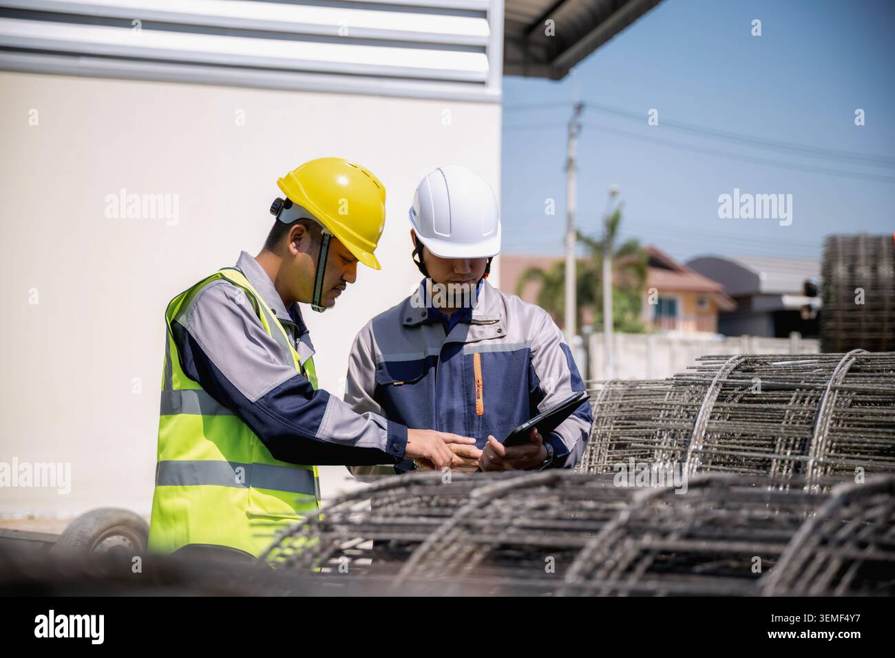 Asian construction workers inspecting steel wire mesh construction site, Two construction workers checking material orders on tablet. They stand near Stock Photo