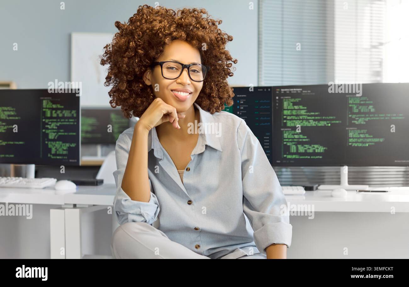 Confident female programmer at computer in modern office, coding on dual screens Stock Photo