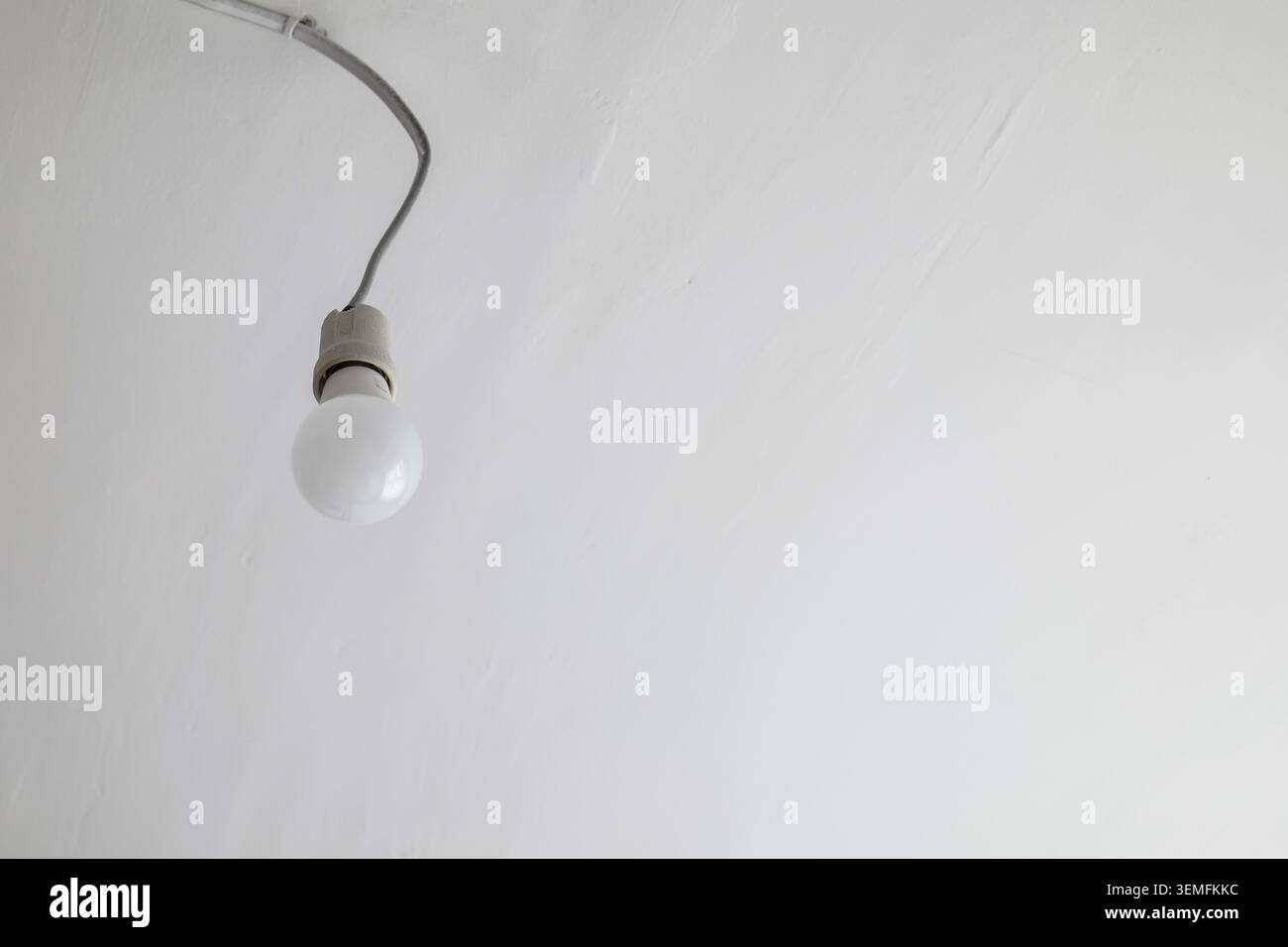 Single light bulb hanging from a wire on a white ceiling Stock Photo