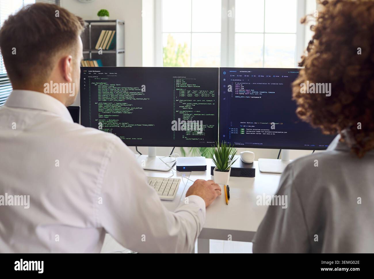 Developers collaborating on code at dual monitors in office, programming team Stock Photo