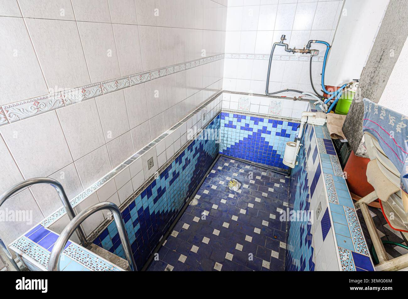 indoor tile-lined pool/tub area with blue and white patterns, plumbing fixtures, and some clutter. It appears somewhat aged and perhaps unused recentl Stock Photo