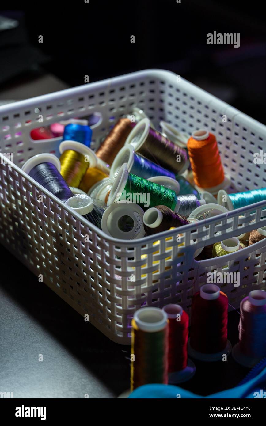 Sewing thread assortment in a white plastic basket in a dark setting Stock Photo