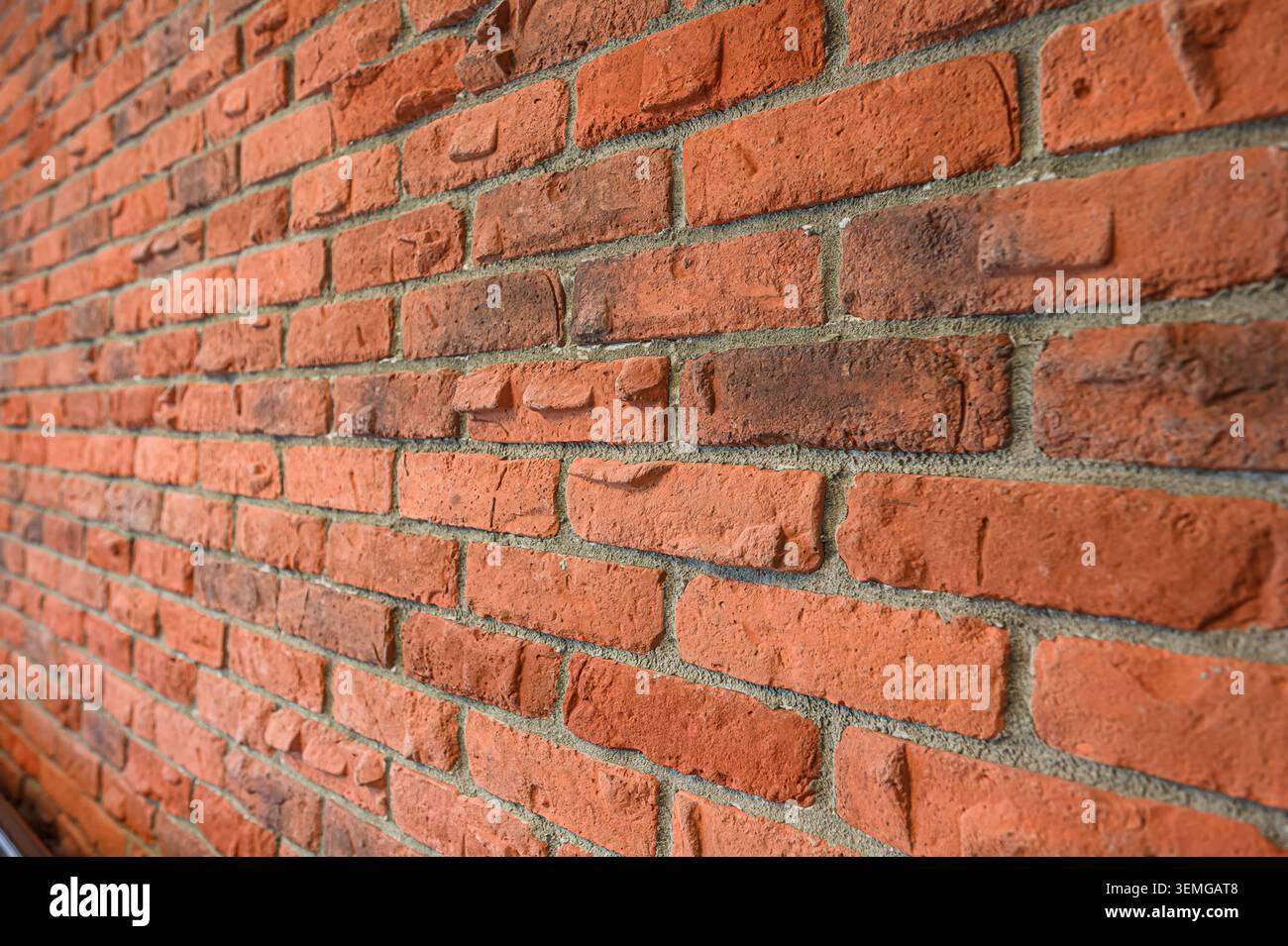 brick wall is shown at an angle. The bricks are predominantly reddish-orange with some darker, mottled sections Stock Photo