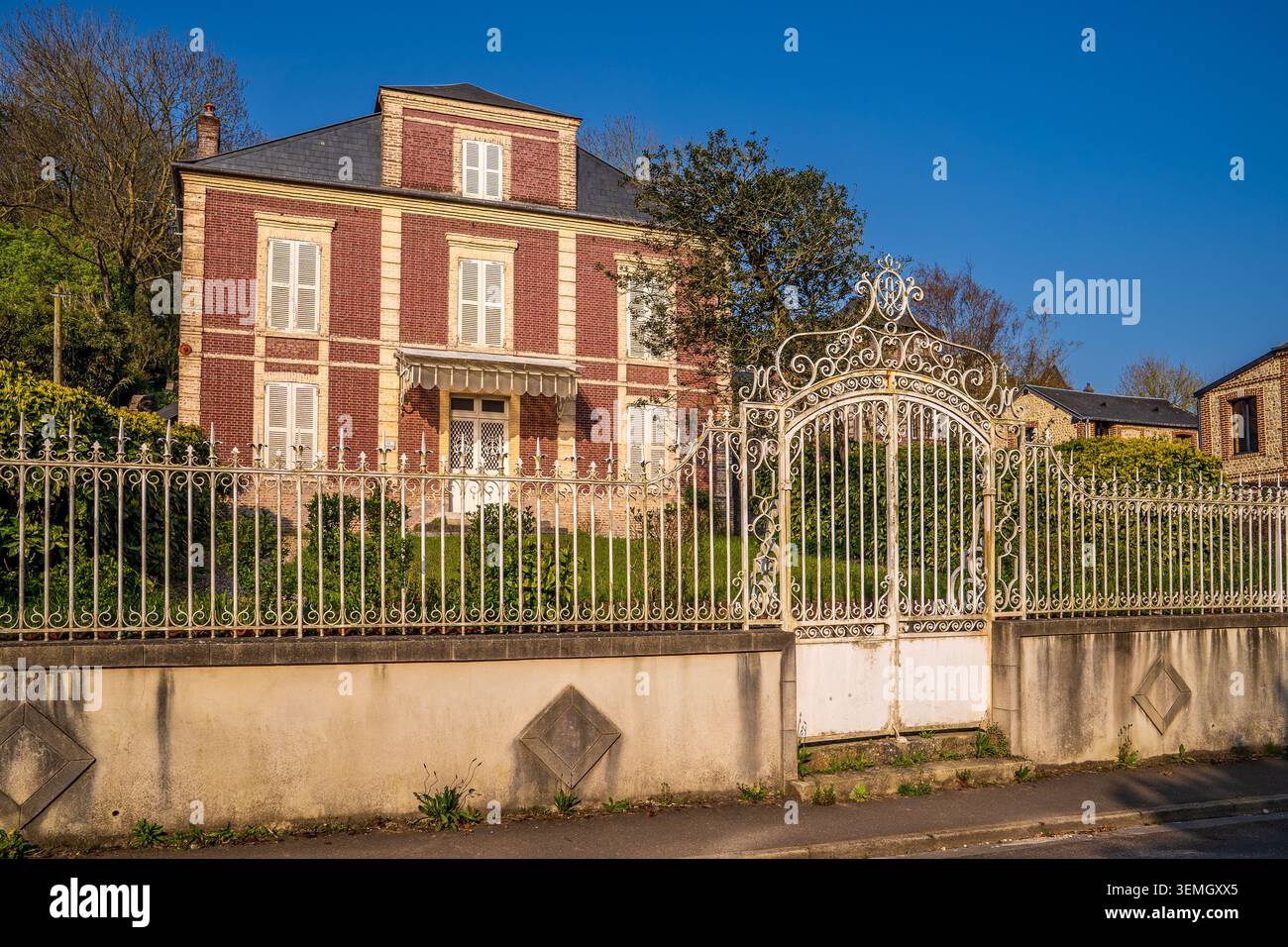 An imposing multi-story period residence stands out for its red brick facade and closed white shutters. The property is protected by an elegant and de Stock Photo