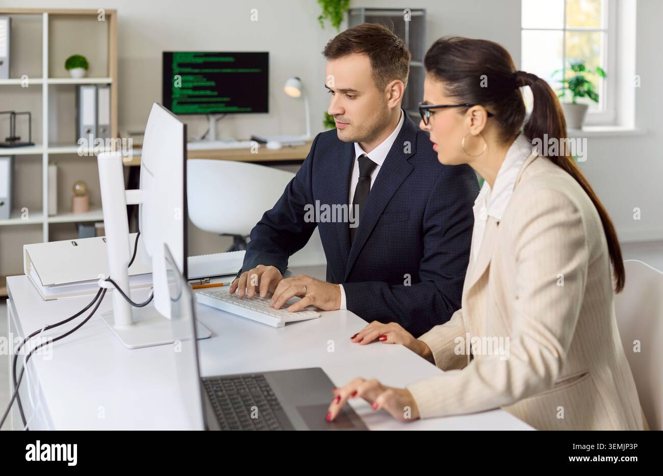 Colleagues collaborating at desktop computers in modern office, coding tasks Stock Photo