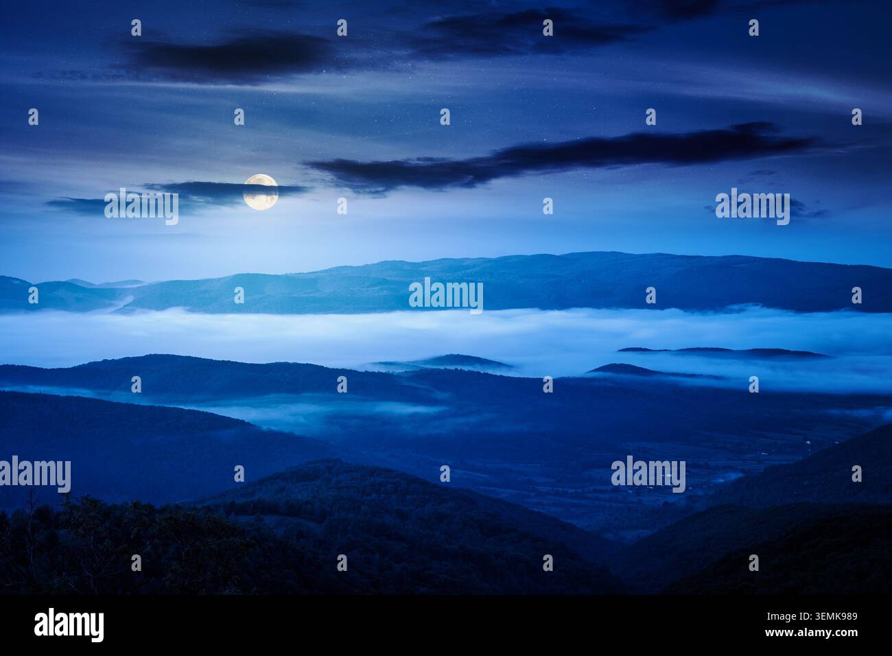 foggy carpathian countryside scenery in summer at night. mysterious view of mountainous landscape with rural fields on rolling hills. full moon over f Stock Photo
