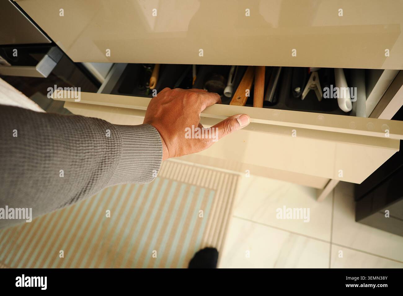 Hand opens drawer with tools in modern kitchen setting Stock Photo