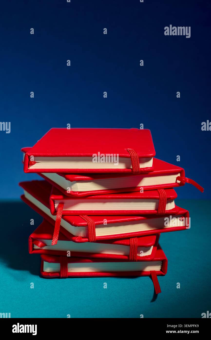 Stack of red notebooks against a bold blue background Stock Photo