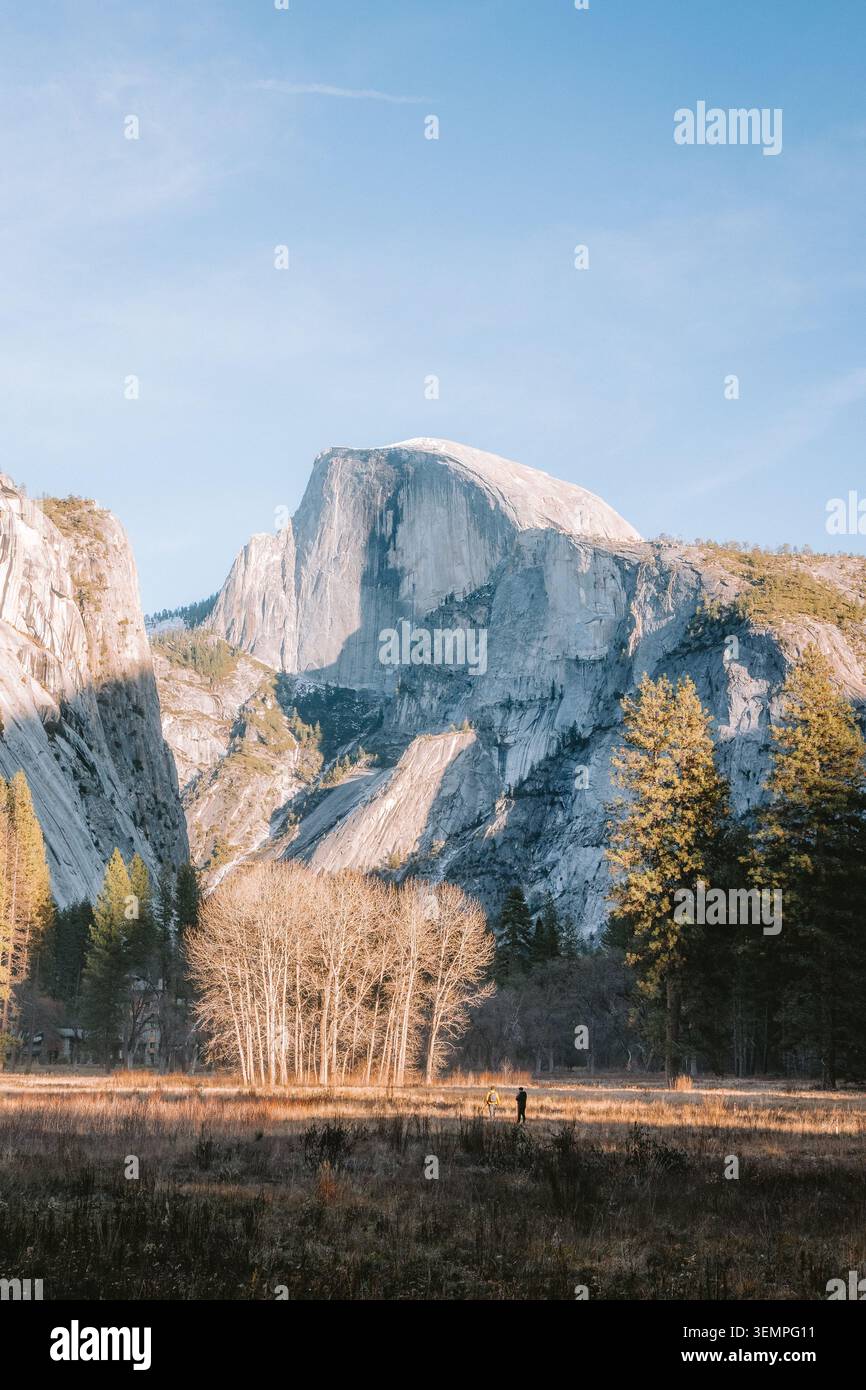 Two people walking in a meadow below Half Dome mountain Stock Photo