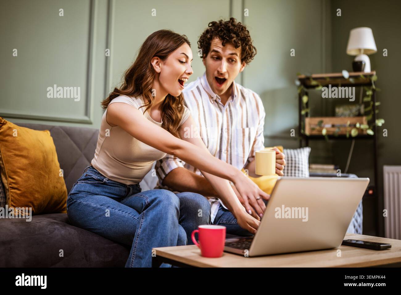 A couple enjoys a relaxed afternoon indoors, reviewing information on a laptop while sharing conversation and coffee. Stock Photo