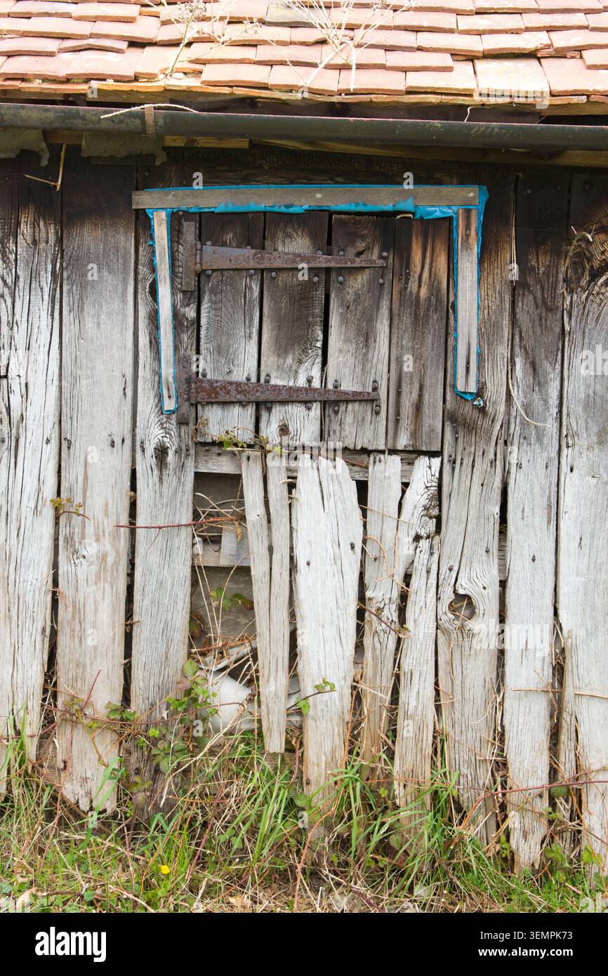 detail of doors and window with rusty hinges on old derelict abandoned wooden stable with attractively split, knotted and grainy old weathered wood Stock Photo
