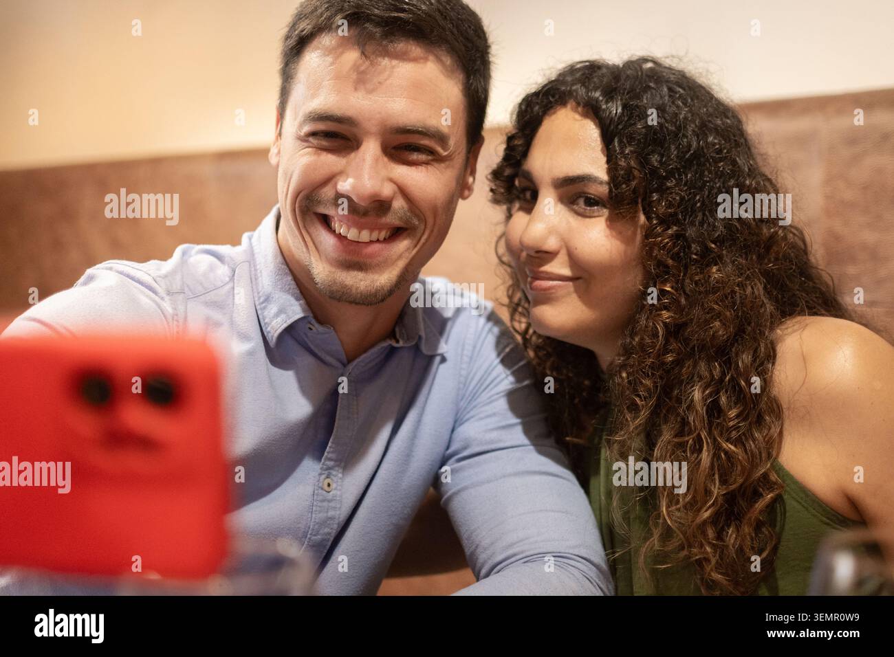 Smiling young couple taking a selfie with a smartphone while enjoying dinner at a restaurant. Modern lifestyle, social media sharing, leisure time, da Stock Photo
