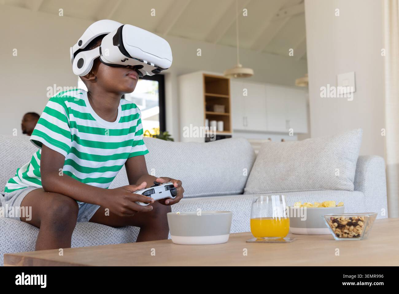 African American family watching preteen boy using white VR headset and holding controller on couch Stock Photo
