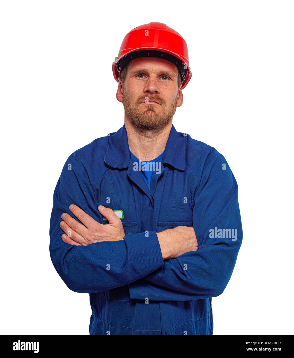 Worker stands with his arms crossed wearing a blue jumpsuit and a red hard hat against a white background. Stock Photo