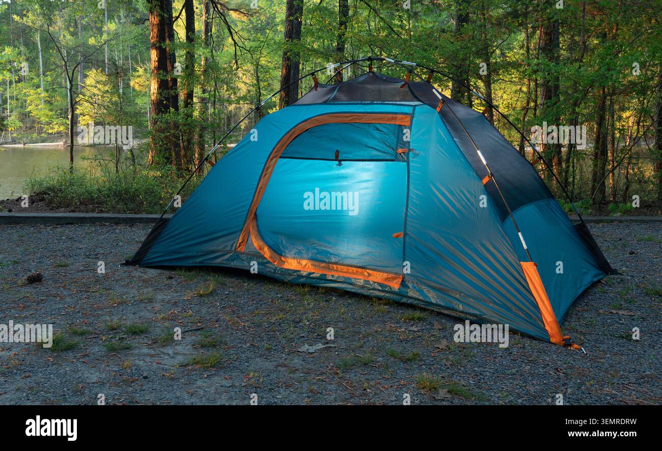 Orange and blue tent set up at a campsite in the trees near a lake ...