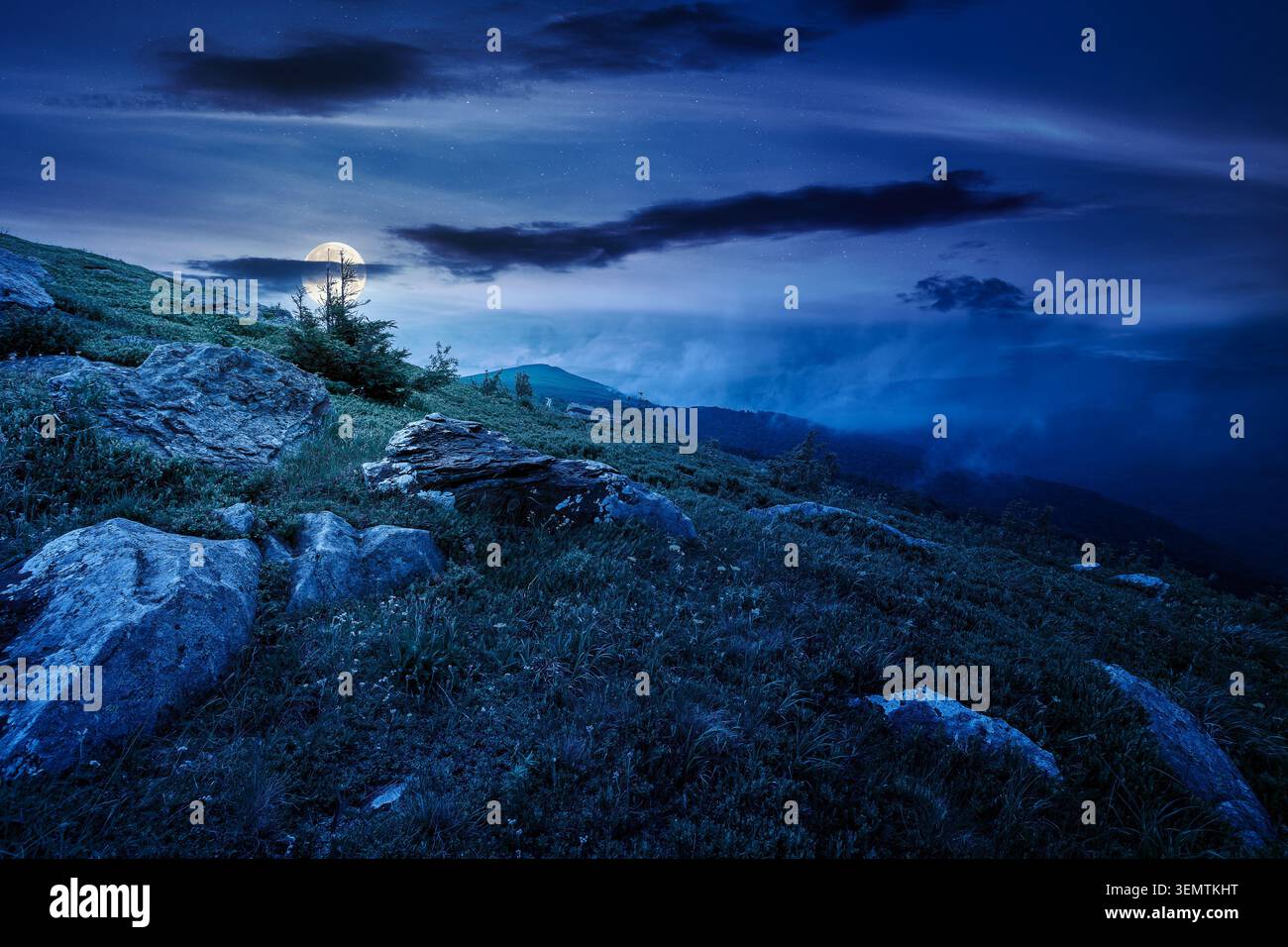 green landscape of mountain in summer at night. mysterious view of rock among grass on the hillside. full moon over travel background under a dark sky Stock Photo