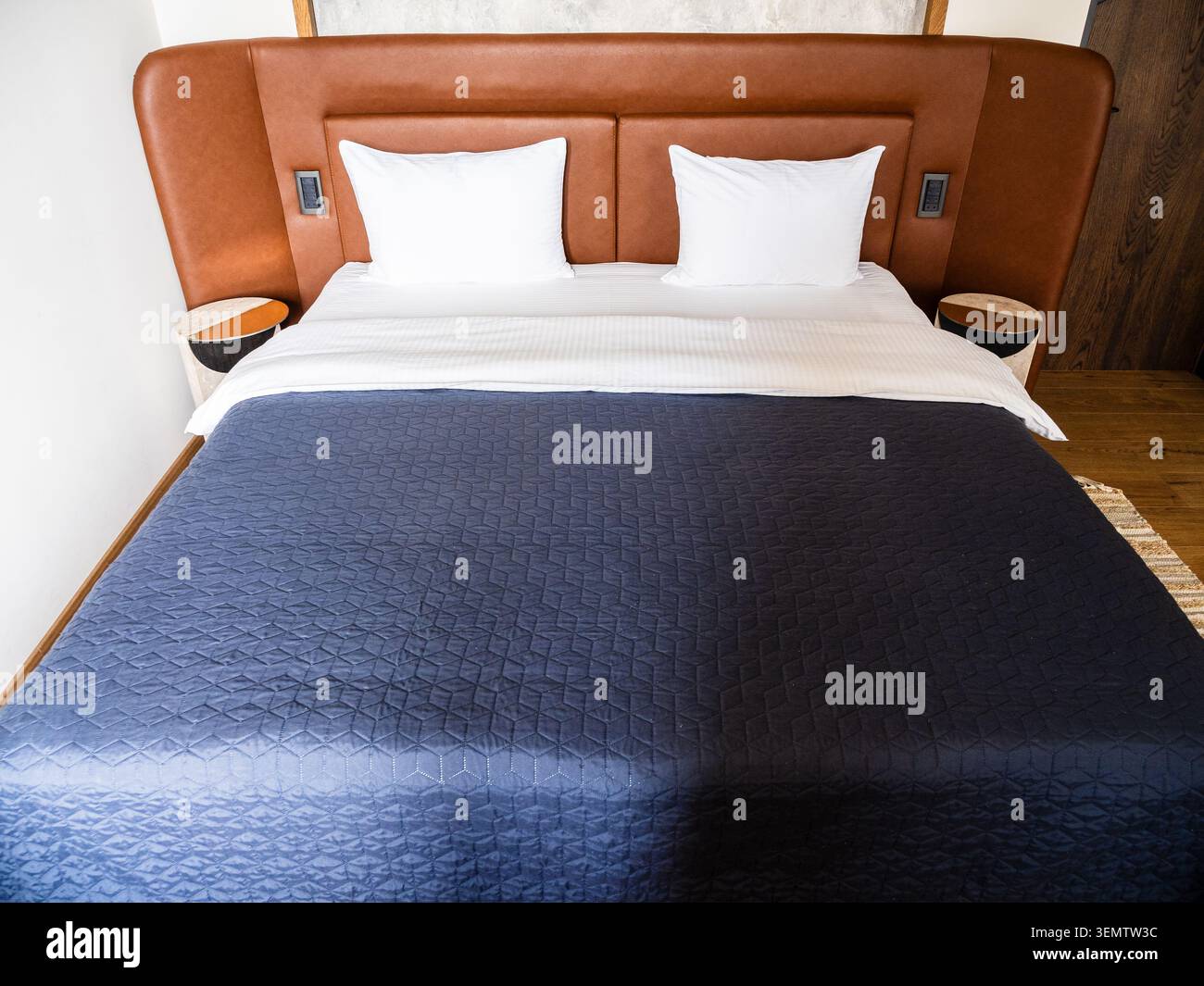 double bed with blue bedspread and leather headboard in hotel room Stock Photo
