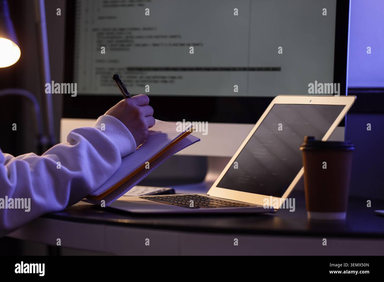 Female programmer's hands writing on notebook in dark office at night Stock Photo