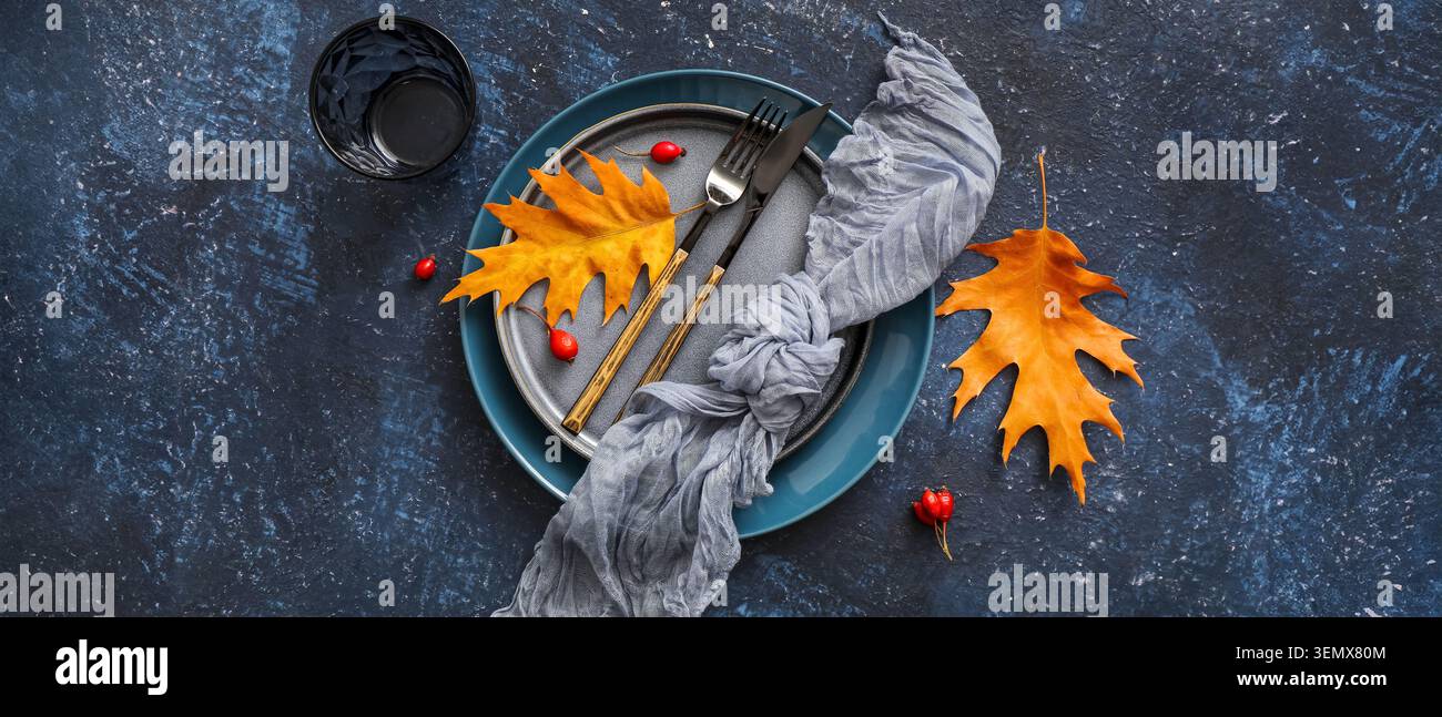 Autumnal table setting with golden oak leaves, berries, and cutlery on dark textured background for seasonal dining Stock Photo