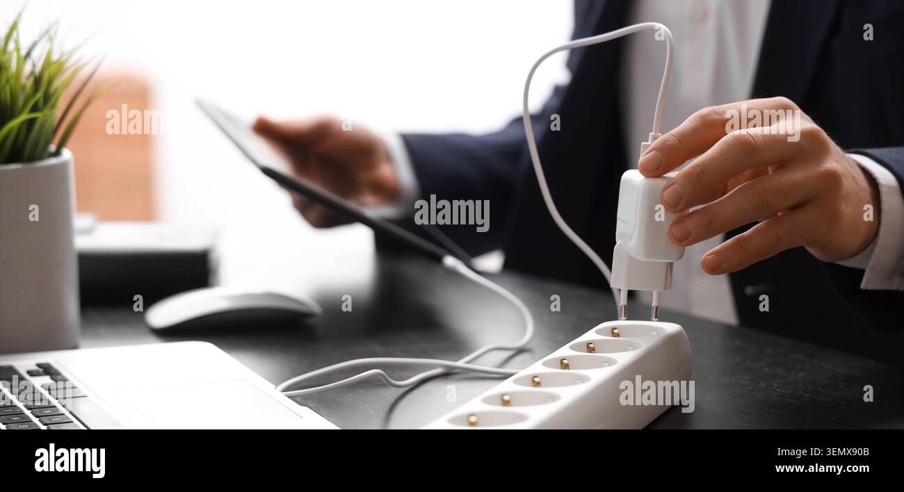 Businessman plugging charger into power strip for tablet, energy consumption and technology integration in modern office Stock Photo