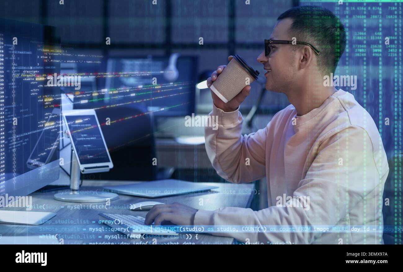 Young male developer drinking coffee while coding on computer, software development and data analysis Stock Photo