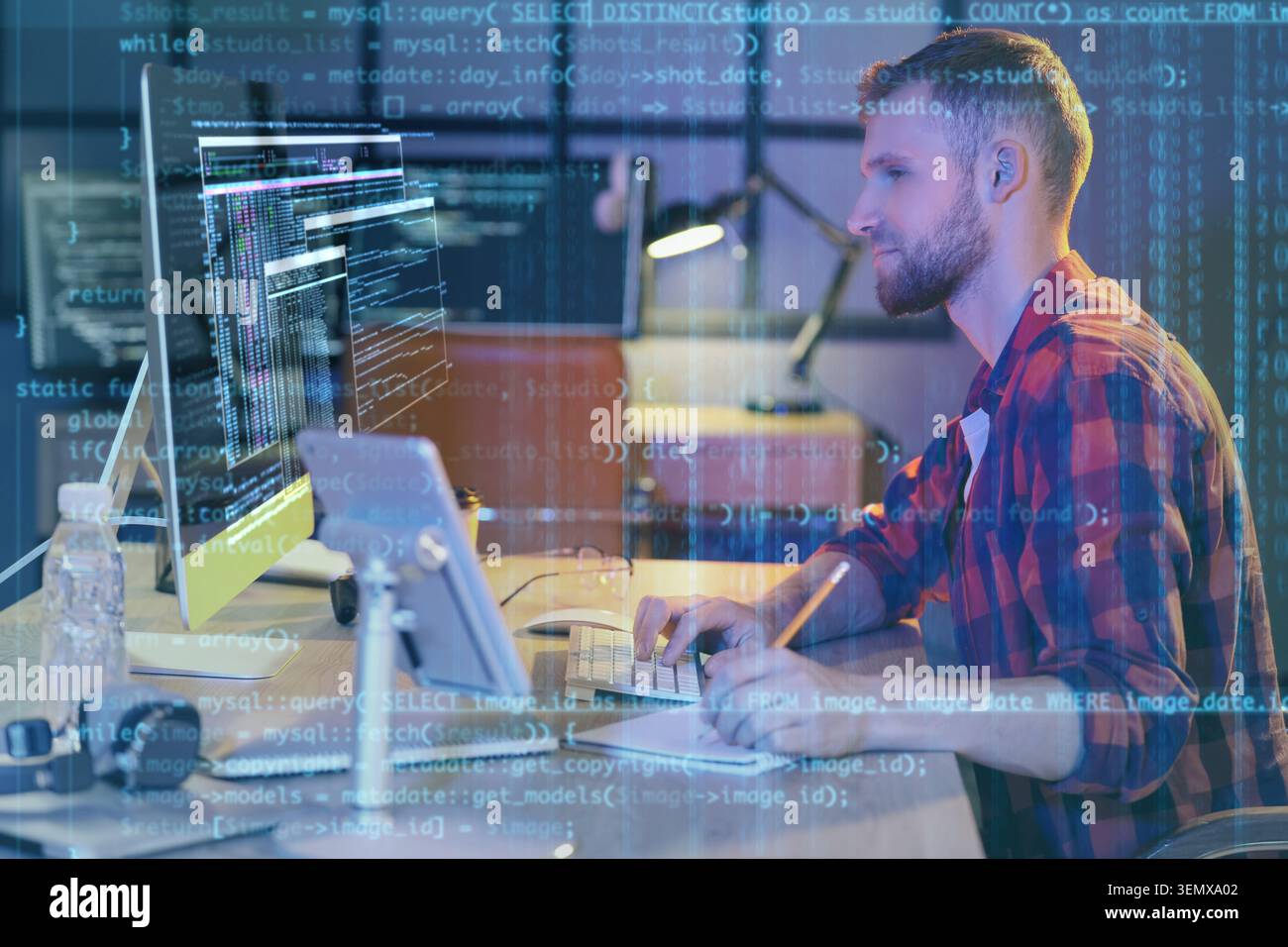 Young male programmer coding software on computer screen with data overlay, digital technology and development Stock Photo