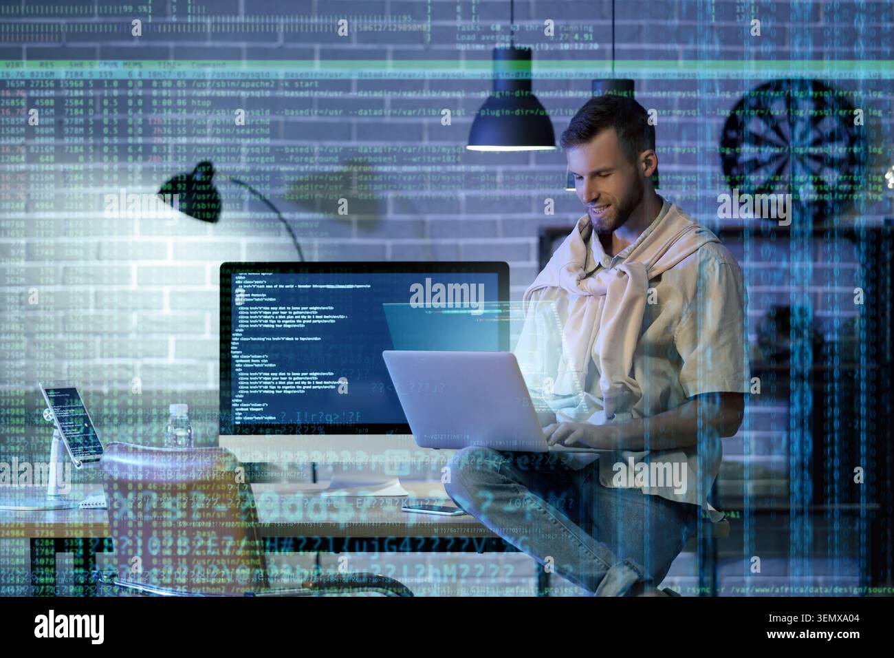Smiling male programmer working on laptop and desktop computer with data overlay, software development and cybersecurity Stock Photo