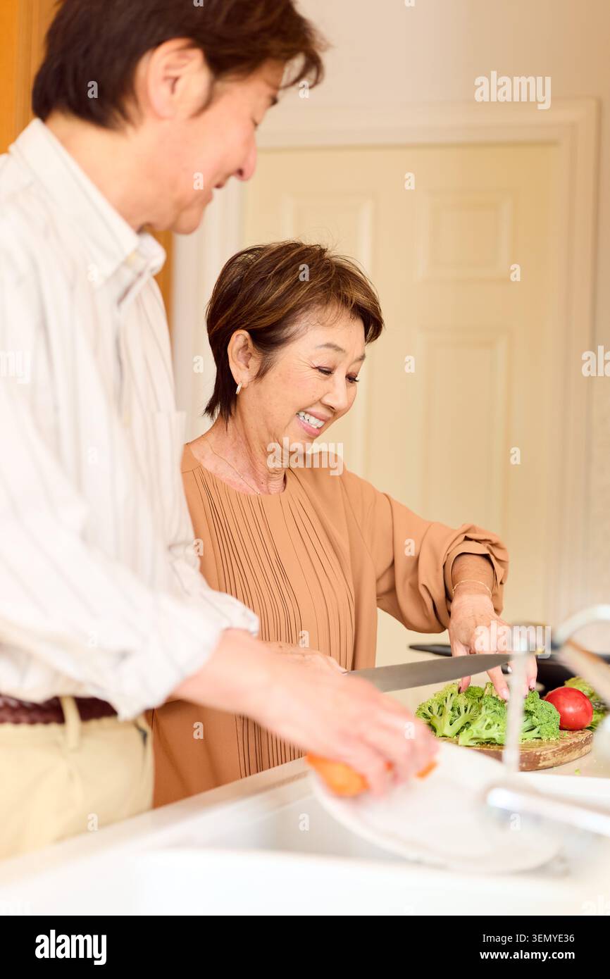Happy Japanese senior couple preparing vegetables in kitchen Stock Photo