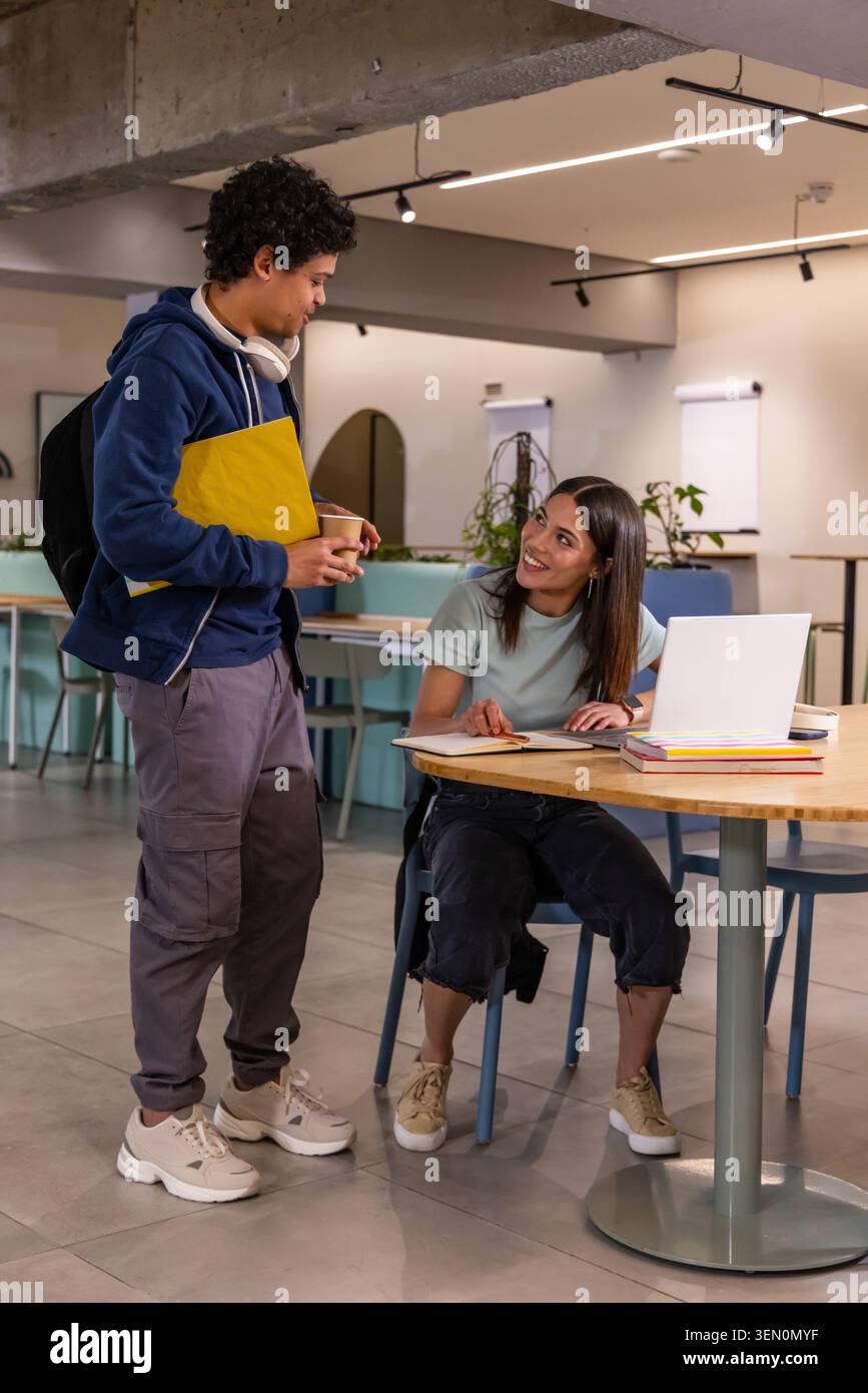 College students studying together in study lounge using laptop, notes, yellow folder, coffee cup Stock Photo