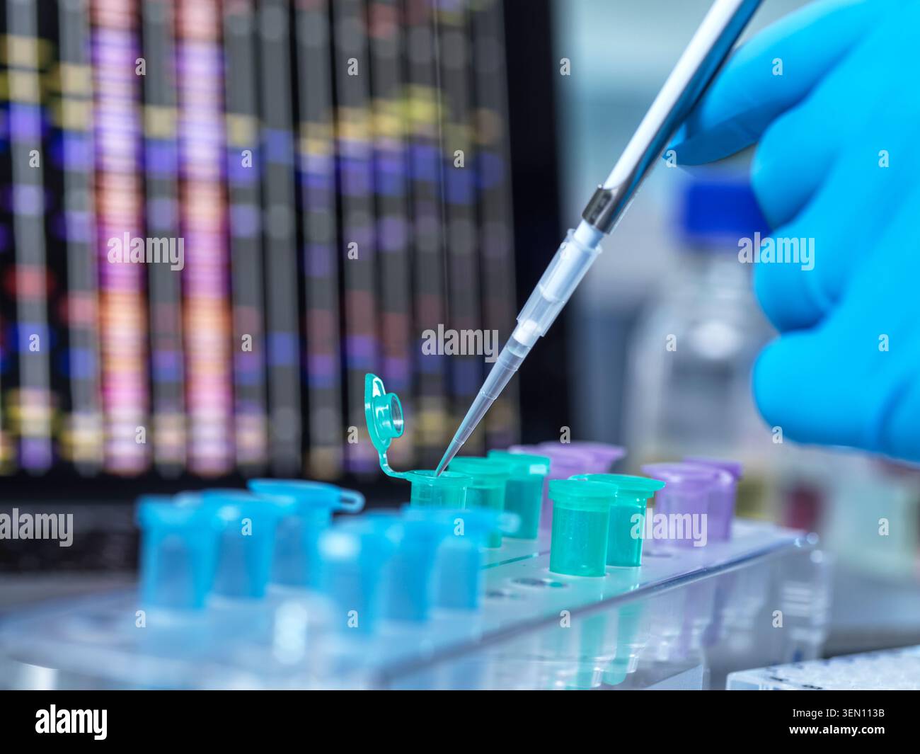 Gloved hand using pipette with colorful test tubes in a lab setting with data screen behind. Stock Photo