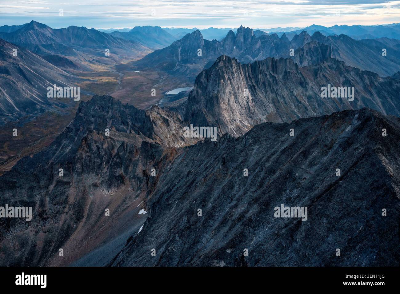 Rugged mountain range under a cloudy sky with sharp peaks and a distant valley. Stock Photo