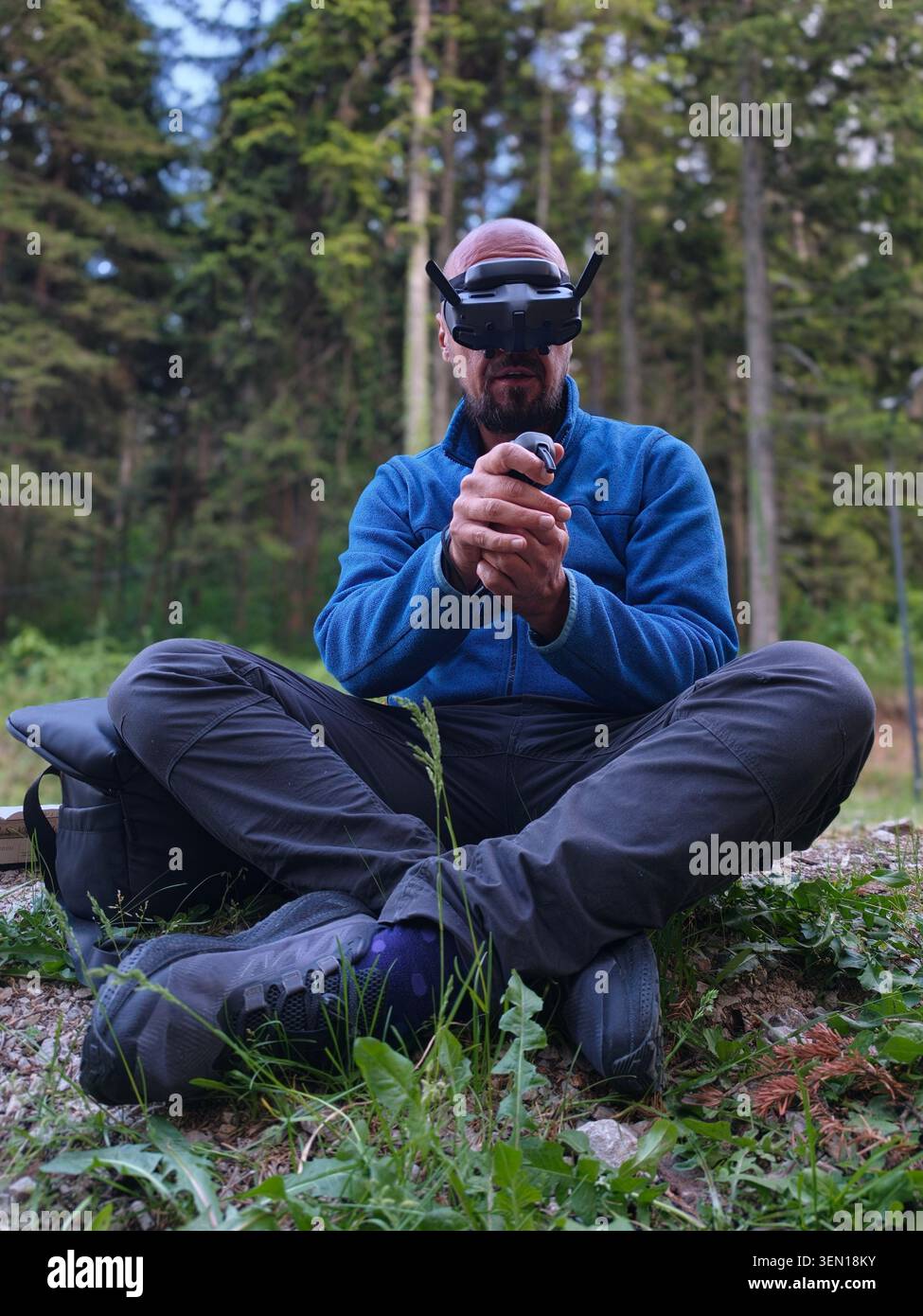 Man Wearing FPV Drone Goggles Using Remote Controller While Sitting in Forest Outdoors Stock Photo