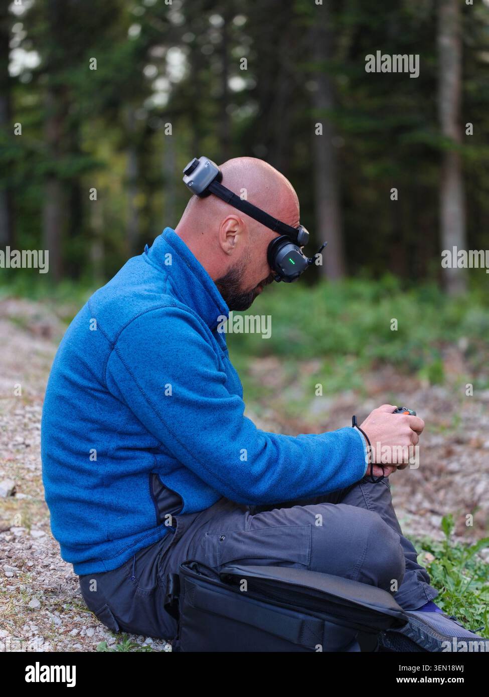 Man Wearing FPV Drone Goggles Sitting Outdoors Controlling Remote Controller in Forest Stock Photo