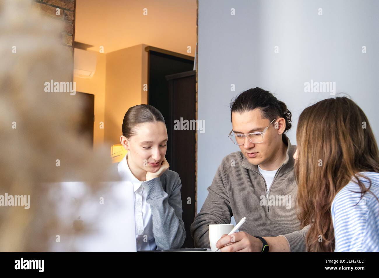Small multi-generation team working together at table, discussing ideas and taking notes. Focused collaboration, problem solving and productive teamwo Stock Photo