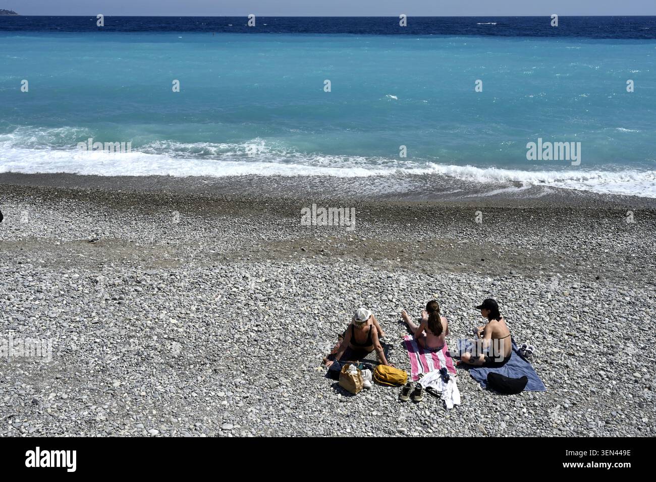 Three women sitting on pebble beach looking out on Mediterranean sea, city of Nice, France Stock Photo