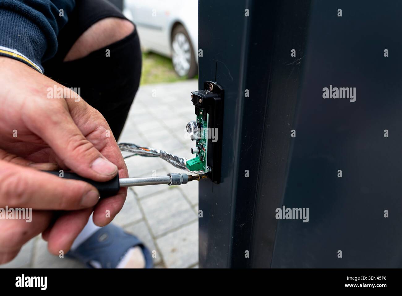 Hand installing an obstacle sensor with network cable wiring on a metal gate post using a screwdriver Stock Photo