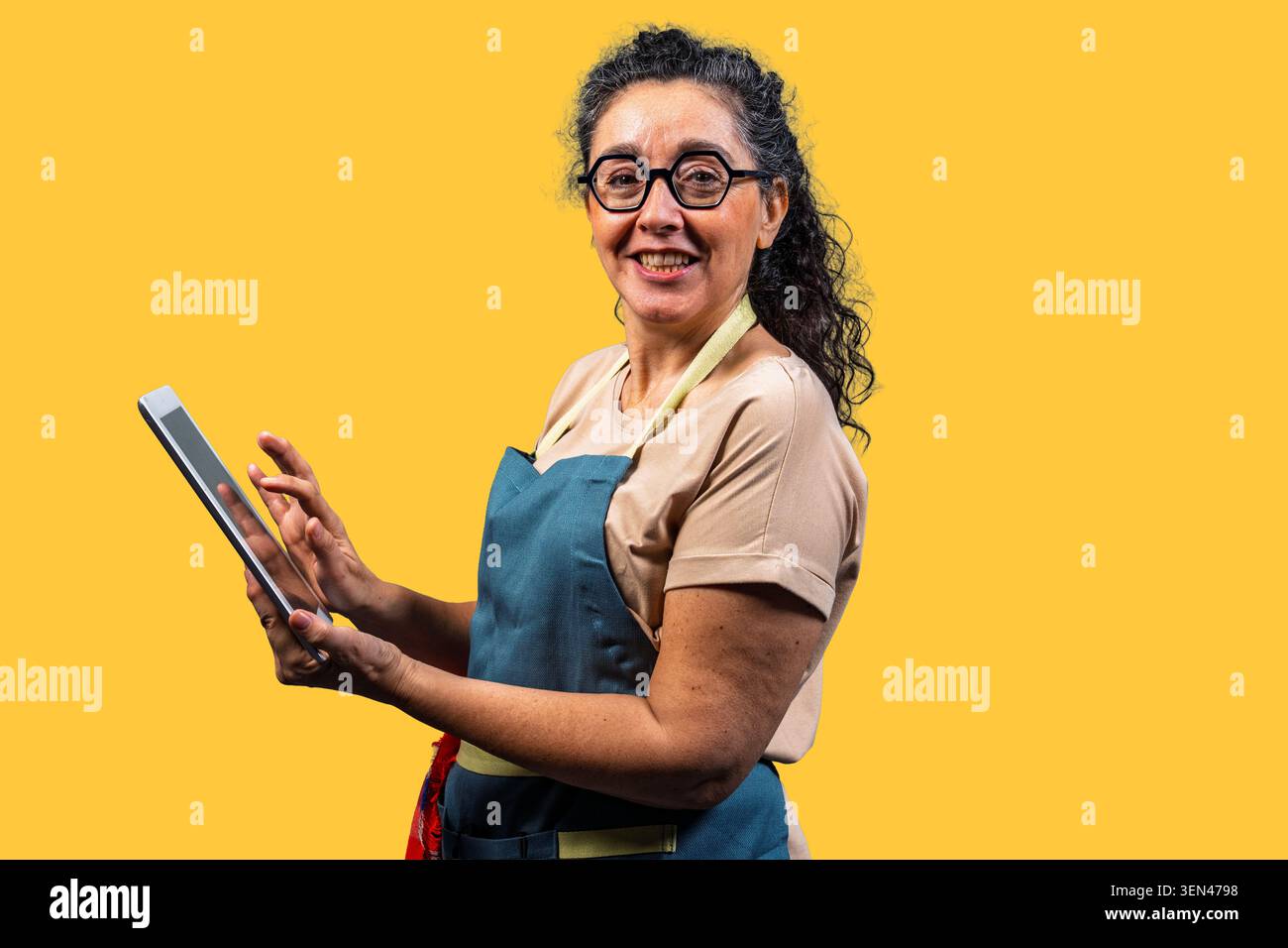Smiling woman small business owner using a tablet for e-commerce on yellow background Stock Photo