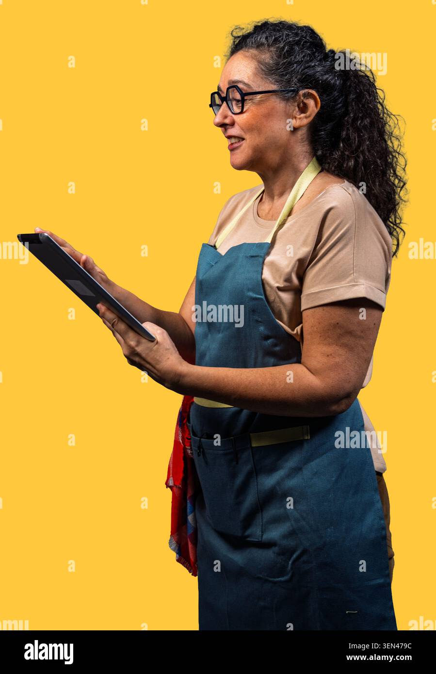 Woman wearing apron and glasses using a tablet, managing her small business Stock Photo