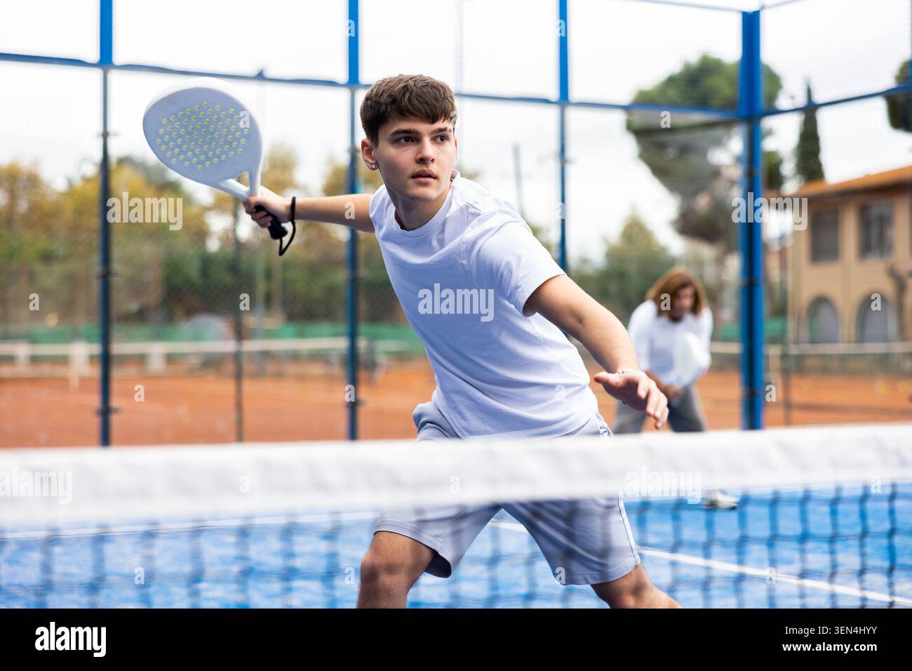 Sportive young man holding padel racquet in hand and ready to return ball while playing in court Stock Photo