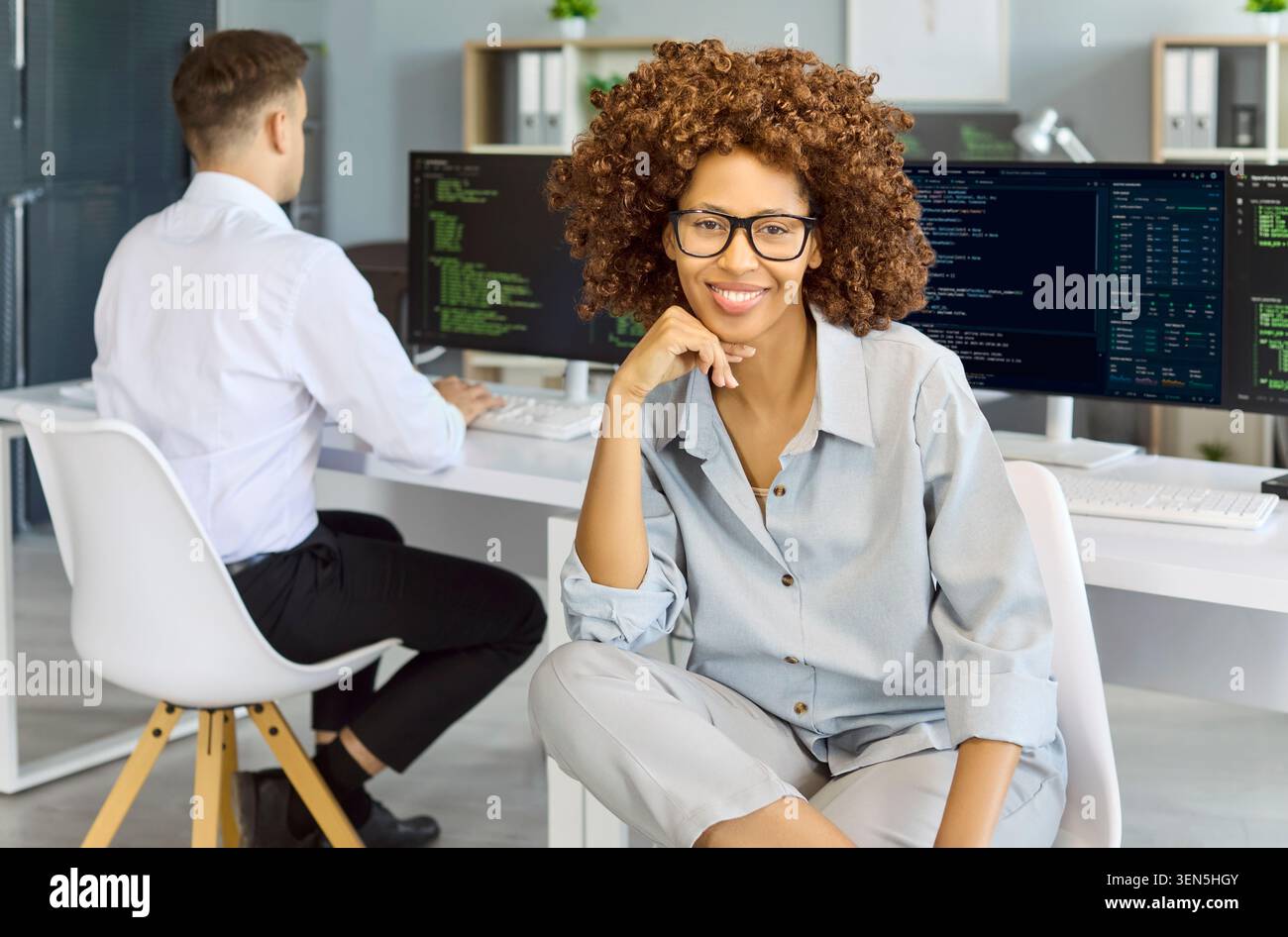 Confident female programmer portrait with code monitors in contemporary office Stock Photo