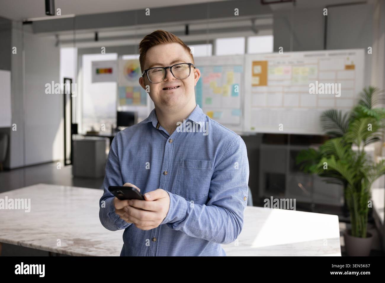 Young man with Down syndrome using smartphone in office Stock Photo