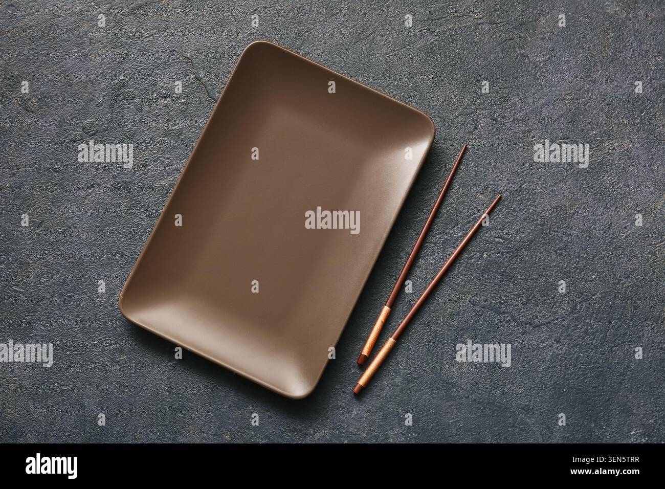 Empty brown rectangular plate with chopsticks on dark textured background, asian cuisine dining Stock Photo