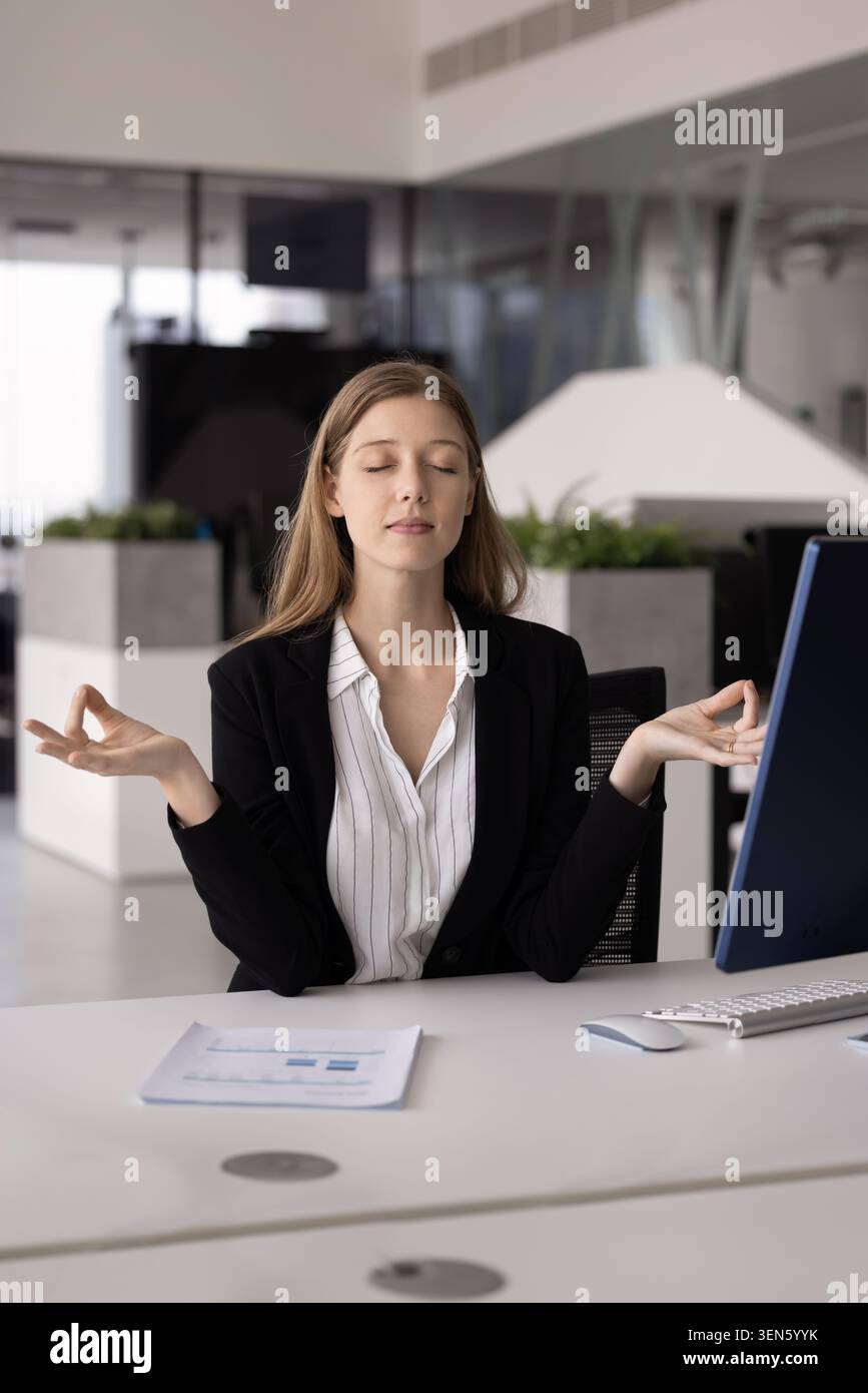 Young woman practicing meditation seated at workplace desk Stock Photo