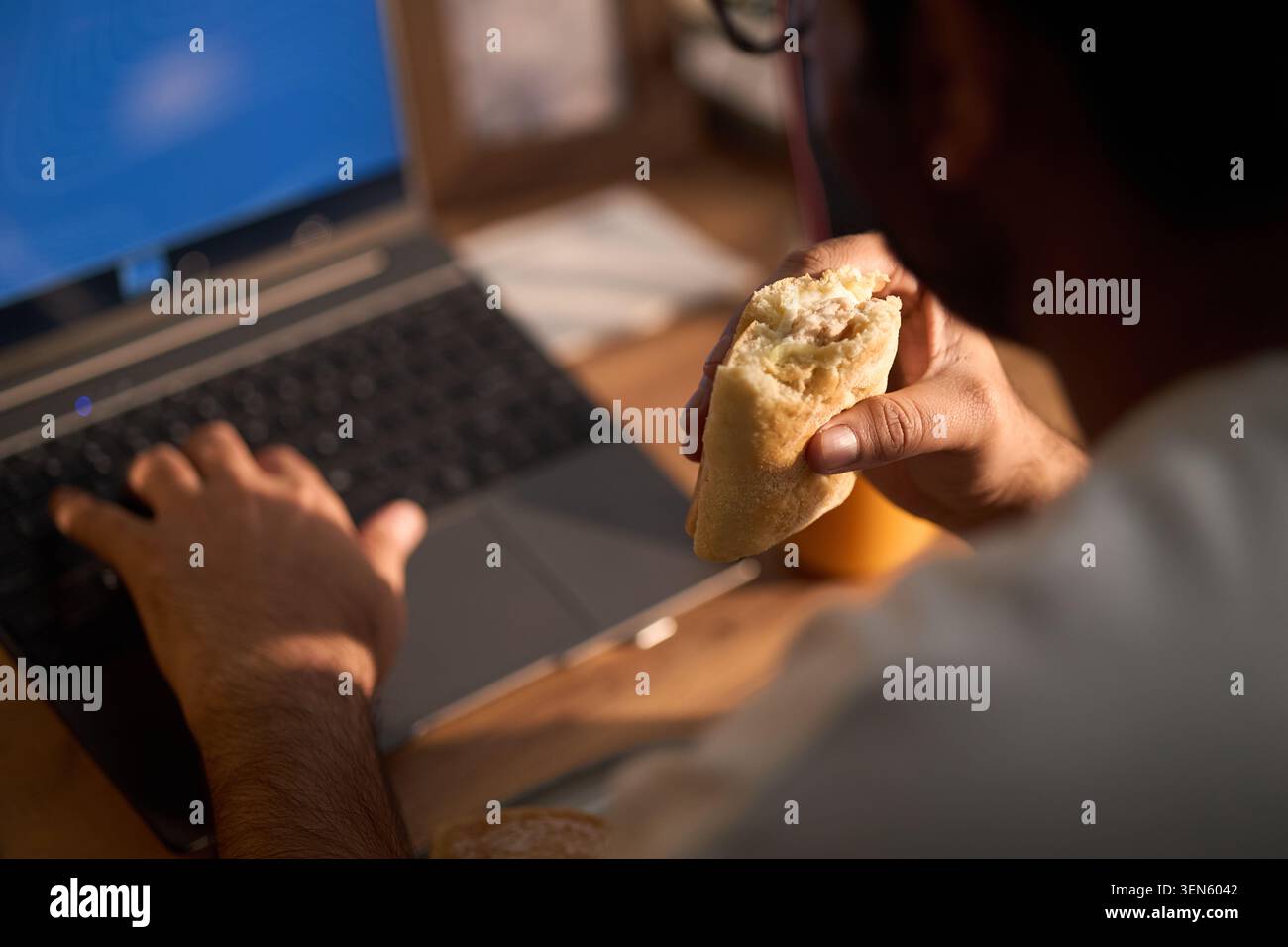 Adult Freelancer Eating While Using Laptop at Home Stock Photo
