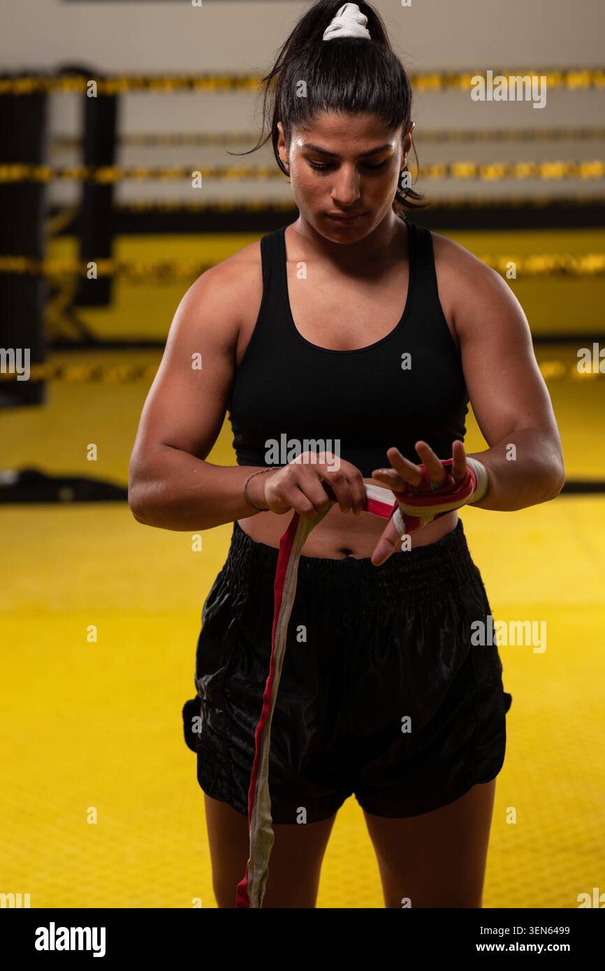 Female Boxer Putting On Hand Wraps in Boxing Ring Preparing For Training Session With Focused Determination Stock Photo