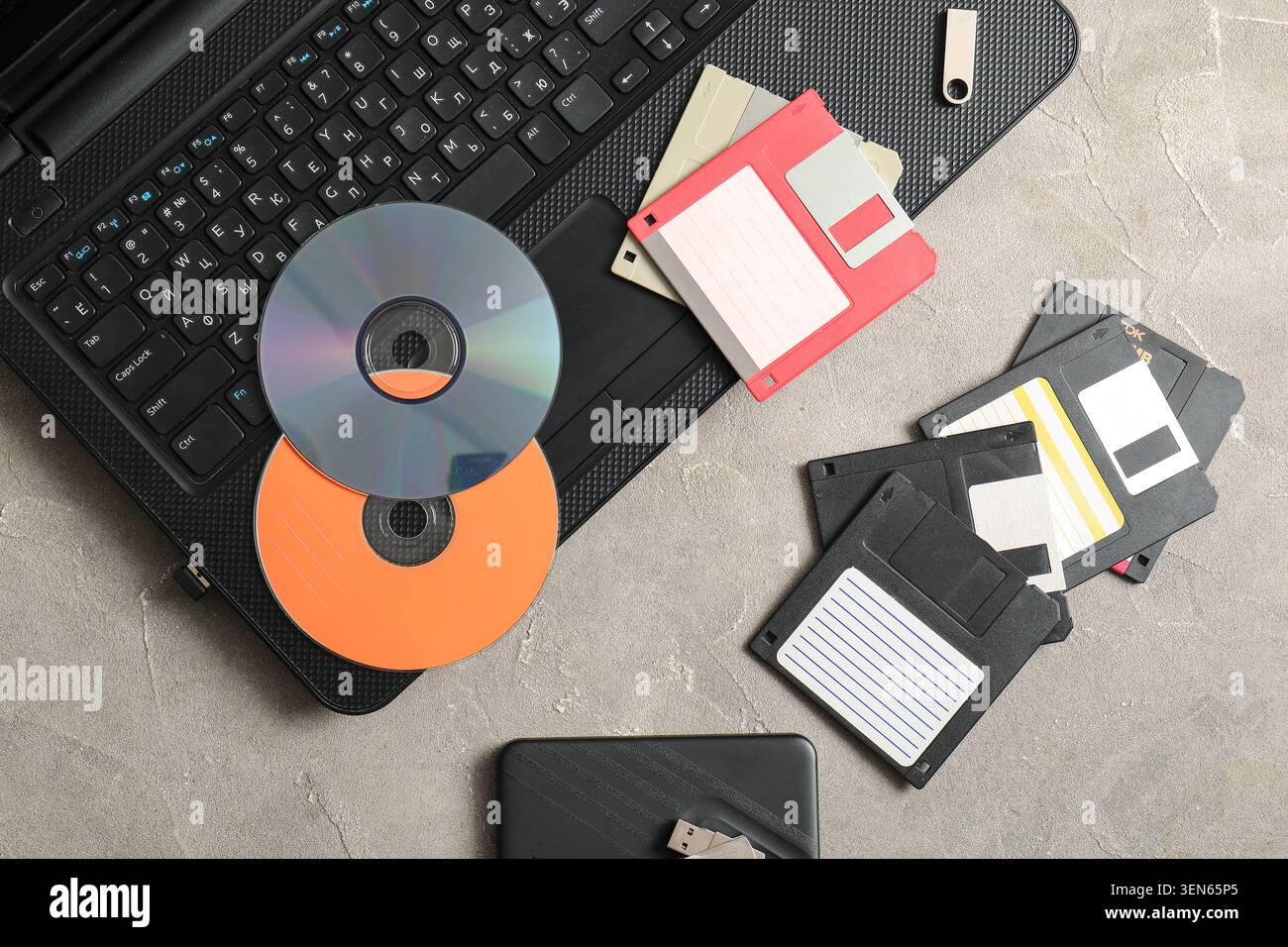 Digital data storage evolution: laptop, USB drive, cds, and floppy disks on concrete background Stock Photo