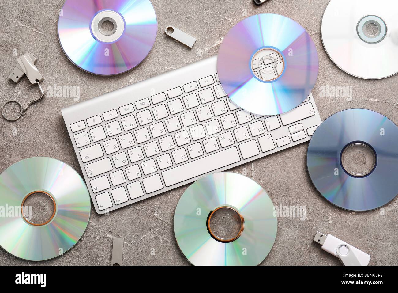 Digital data storage and computer peripherals flat lay with keyboard, cds, and USB drives on gray background Stock Photo