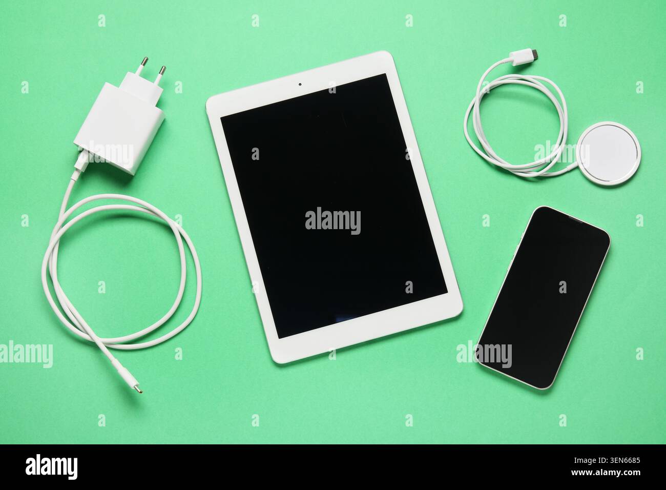 Modern digital tablet, smartphone, charger, and wireless charging pad on green background for technology and connectivity Stock Photo