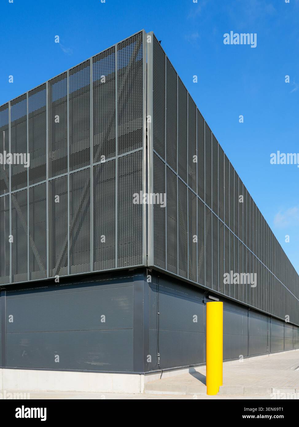 Low-angle view of a contemporary logistics warehouse corner featuring metal mesh cladding and safety bollard Stock Photo