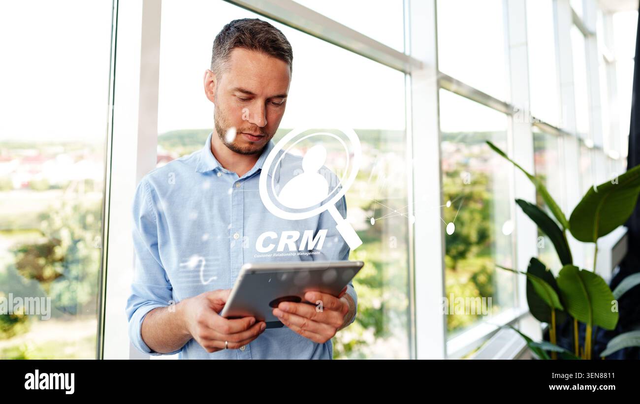 Man using tablet to manage customer data in a bright office with CRM displayed Stock Photo